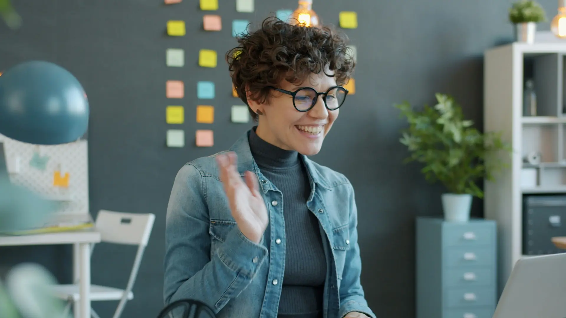 Woman waving hello in front of laptop