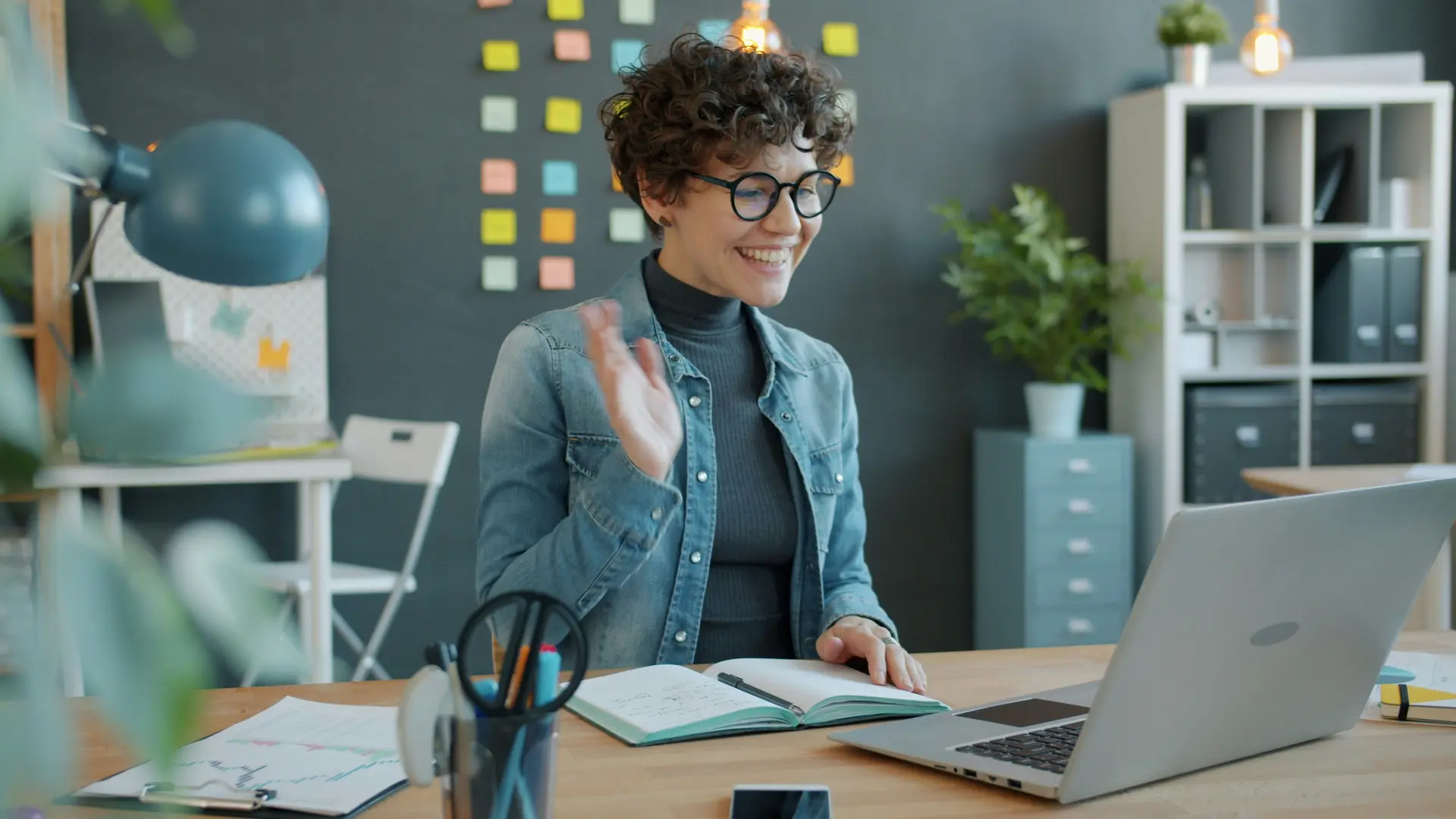 Woman waving hello in front of laptop